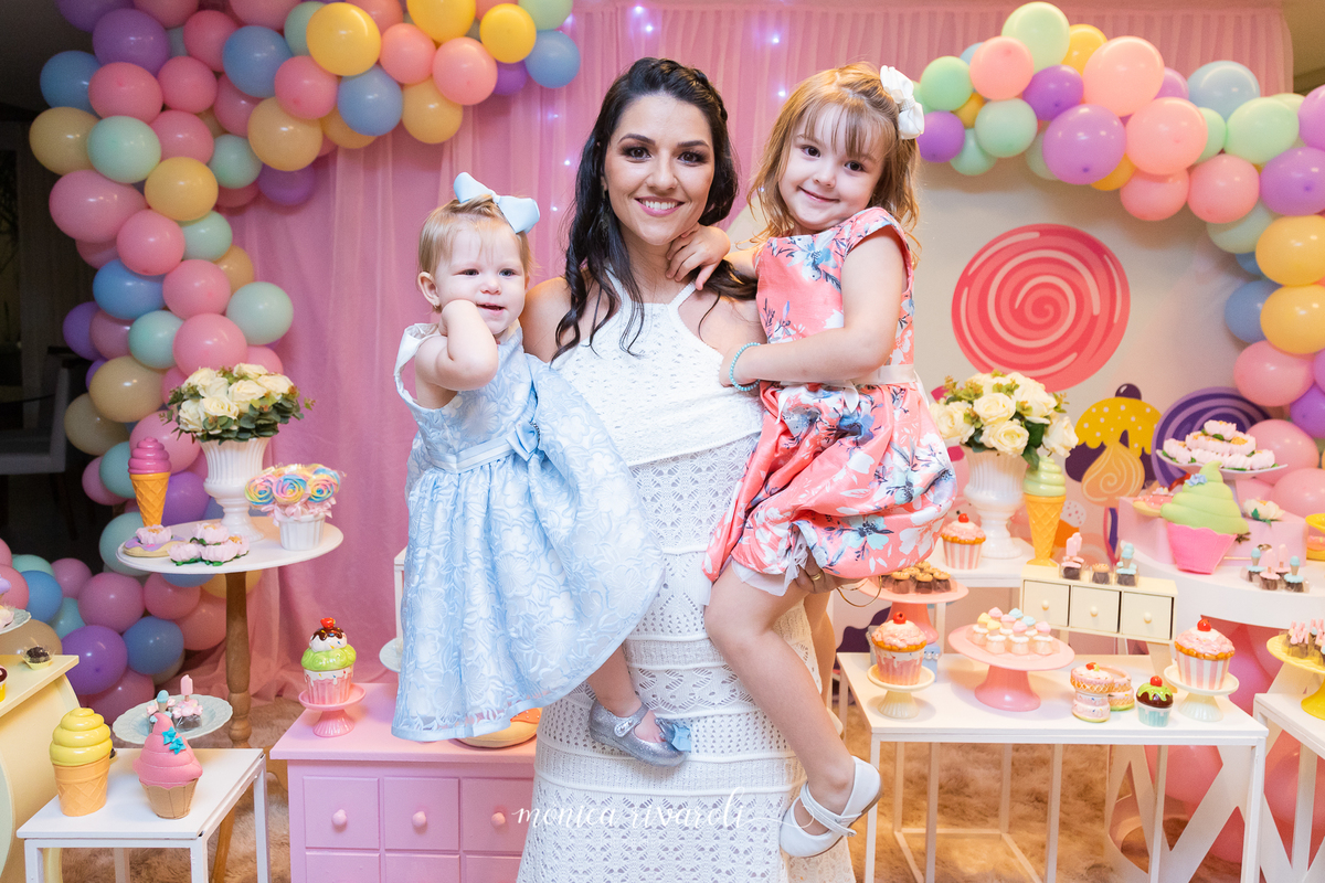 A mãe da Mariah, a segura no colo junto com sua irmãzinha mais velha, a Catarina. Elas sorriem