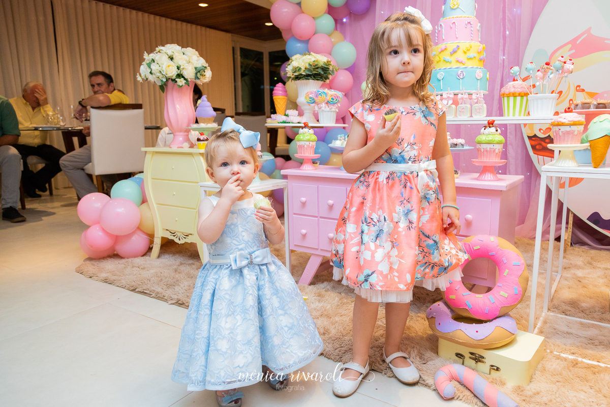 Mariah à frente da mesa de doces ao lado da irmãzinha.