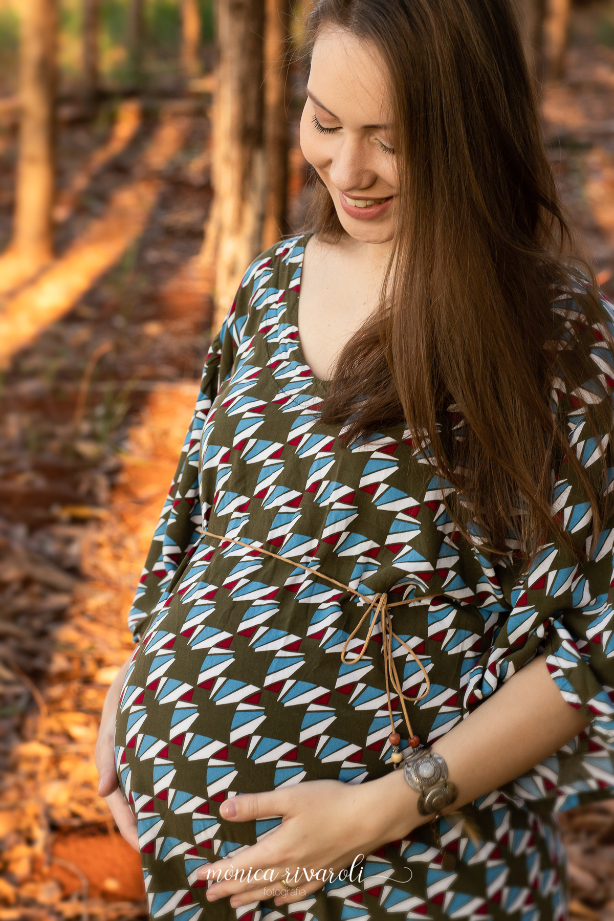 Ainda no mesmo cenário, a mamãe está com as mãos na barriga. Ela está olhando para a barriga com um sorriso.
Fotografado por Mônicas Fotografia em Maringá-PR