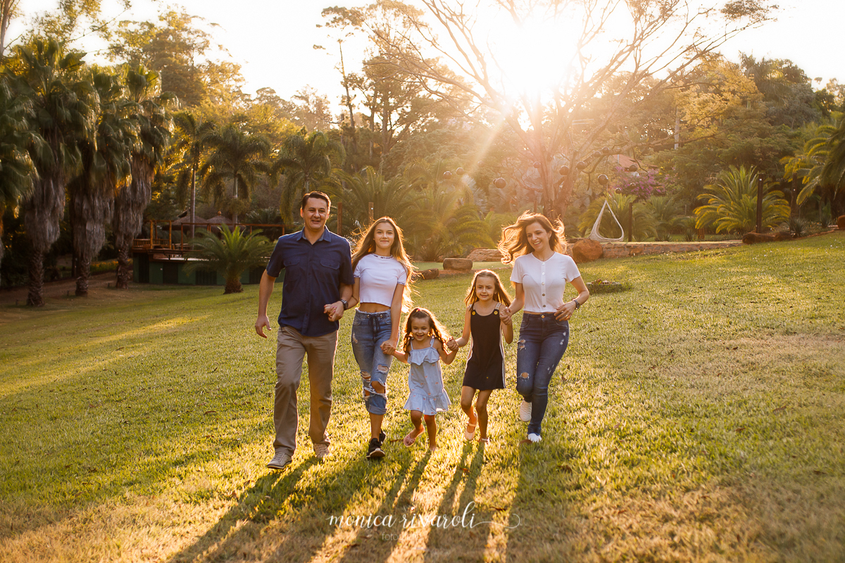 A família corre de mãos dadas nessa foto, o pai na ponta esquerda, ao seu lado a mais velha, a caçula ao meio, a do meio e na ponta direita a mãe. Ao fundo o sol brilha, deixando rastro de luz entre eles e iluminação.