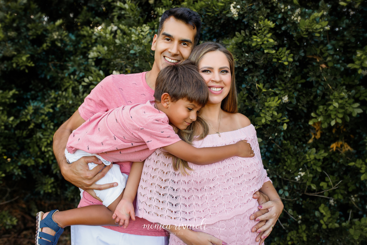 Ainda no mesmo cenário, os pais estão olhando para a frente e o filho mais velho para a barriga. O irmão está no colo do pai abraçando a mãe, que está com as mãos na barriga.
Ensaio Gestante
Fotografado por Mônicas Fotografia em Maringá-PR