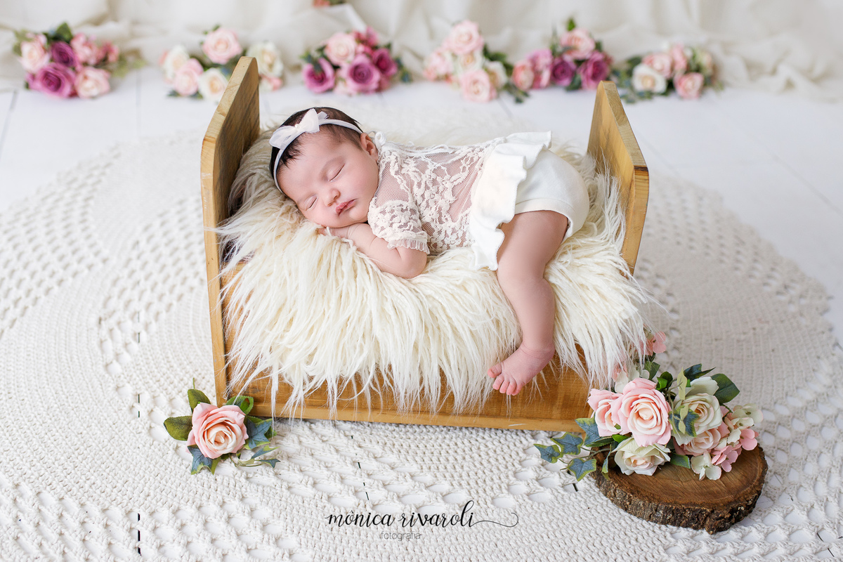 Em um cenário branco com flores em tons de rosa no fundo, a bebê está deitada em uma pequena cama no centro da foto.
Ensaio Newborn
Fotografado por Mônicas Fotografia em Maringá-PR