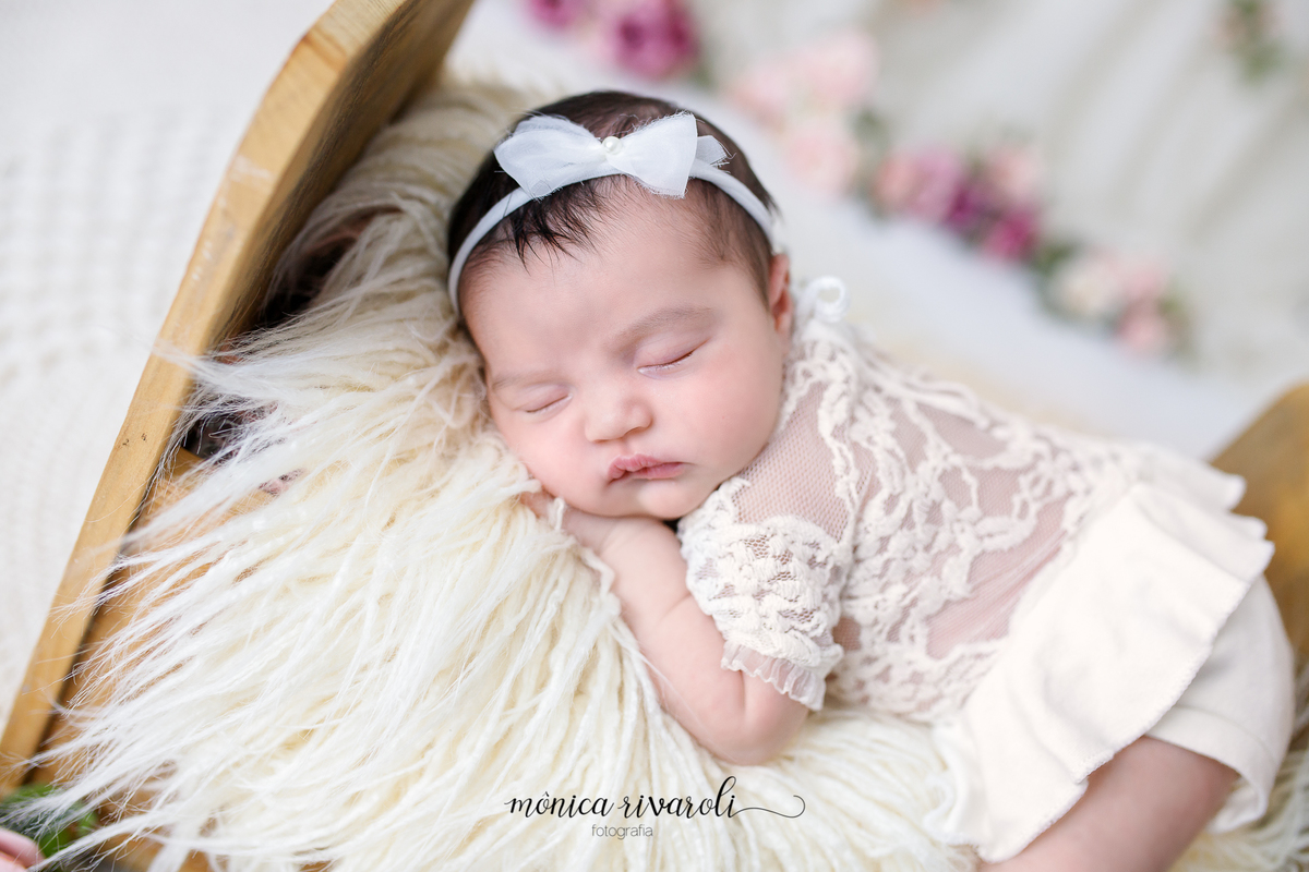 A bebê está dormindo de bruço em uma pequena cama. Ela tem um laço branco na cabeça e está com uma roupa branca.
Ensaio newborn
Fotografado por Mônicas Fotografia em Maringá-PR