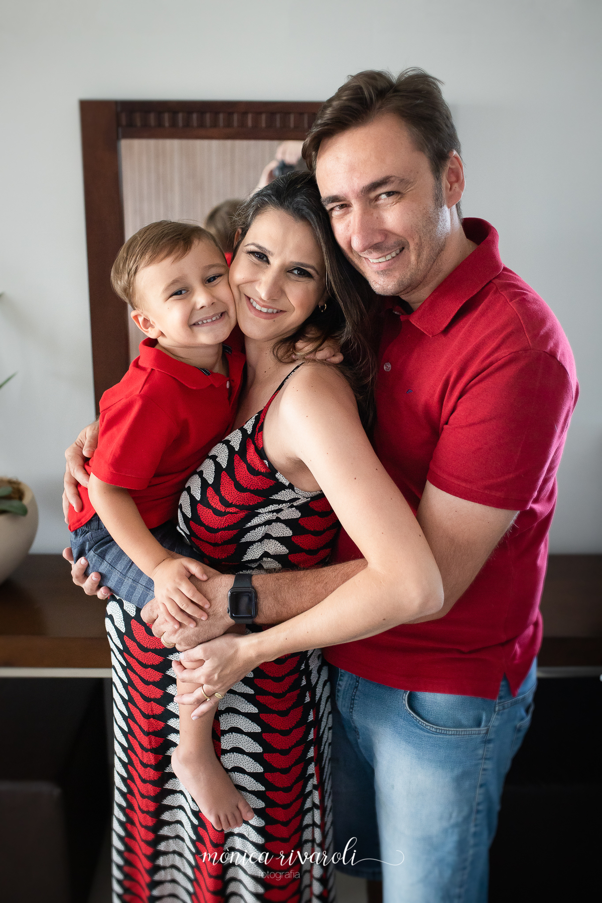 A mãe grávida, o pai e o filho mais velho estão abraçados e sorrindo. A mãe está com o filho mais velho no colo
Fotografado por Mônicas Fotografia em Maringá-PR