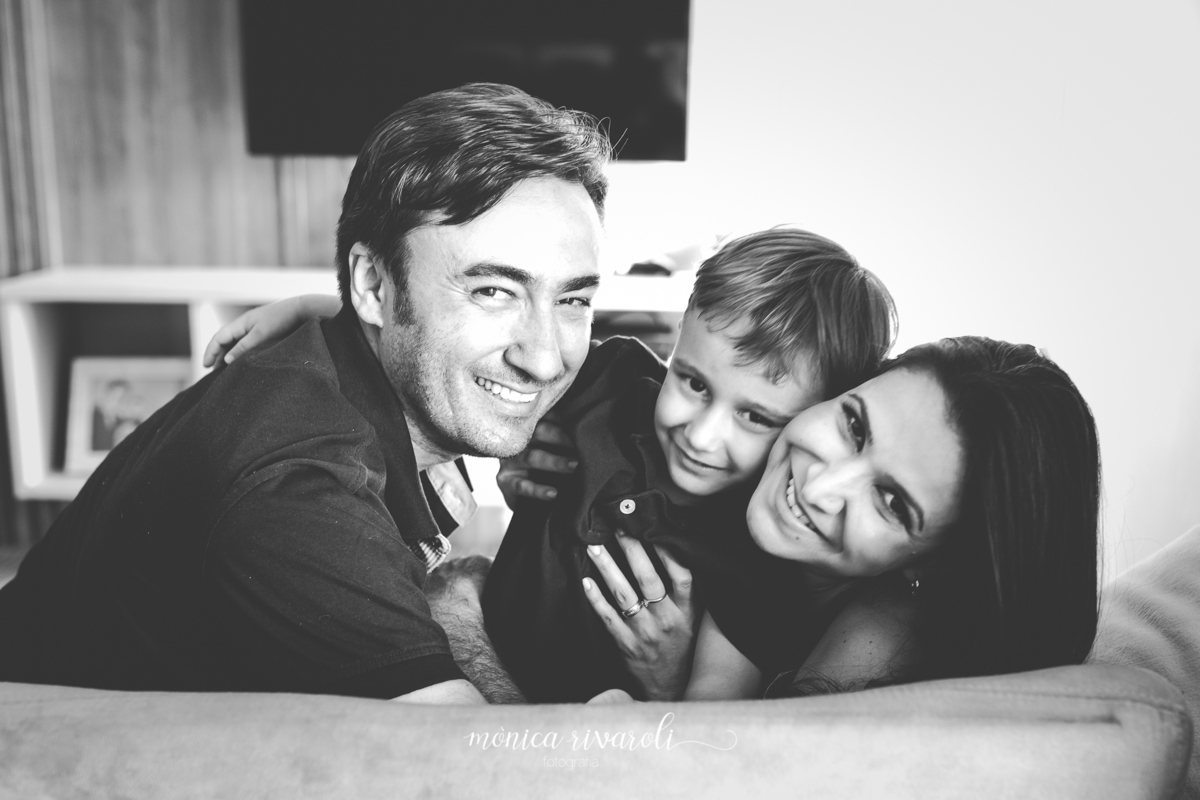 A família está sentada no sofá. O filho mais velho está sentado no meio dos pais e estão todos sorrindo
Fotografado por Mônicas Fotografia em Maringá-PR