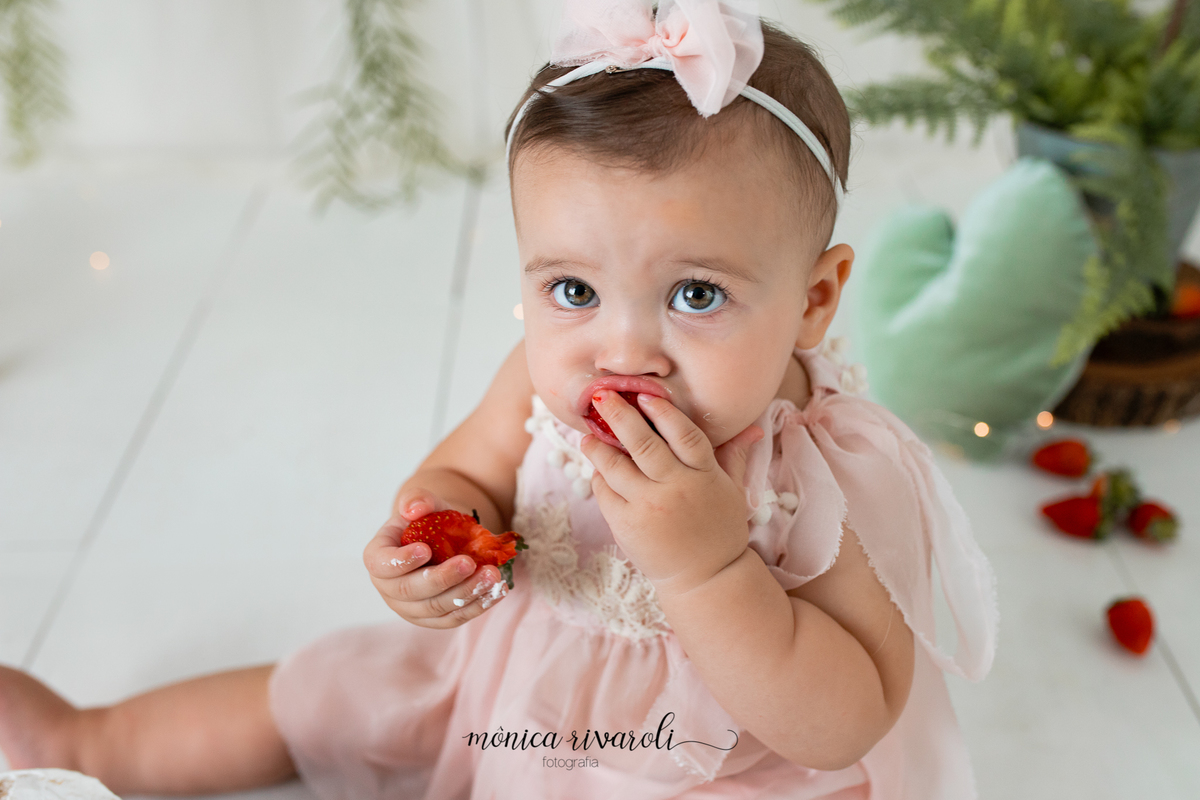 No cenário de Smash, a bebê está segurando um morango quanto come outro. Ela está olhando para a câmera.
Ensaio Smash The Cake
Fotografado por Mônicas Fotografia em Maringá-PR