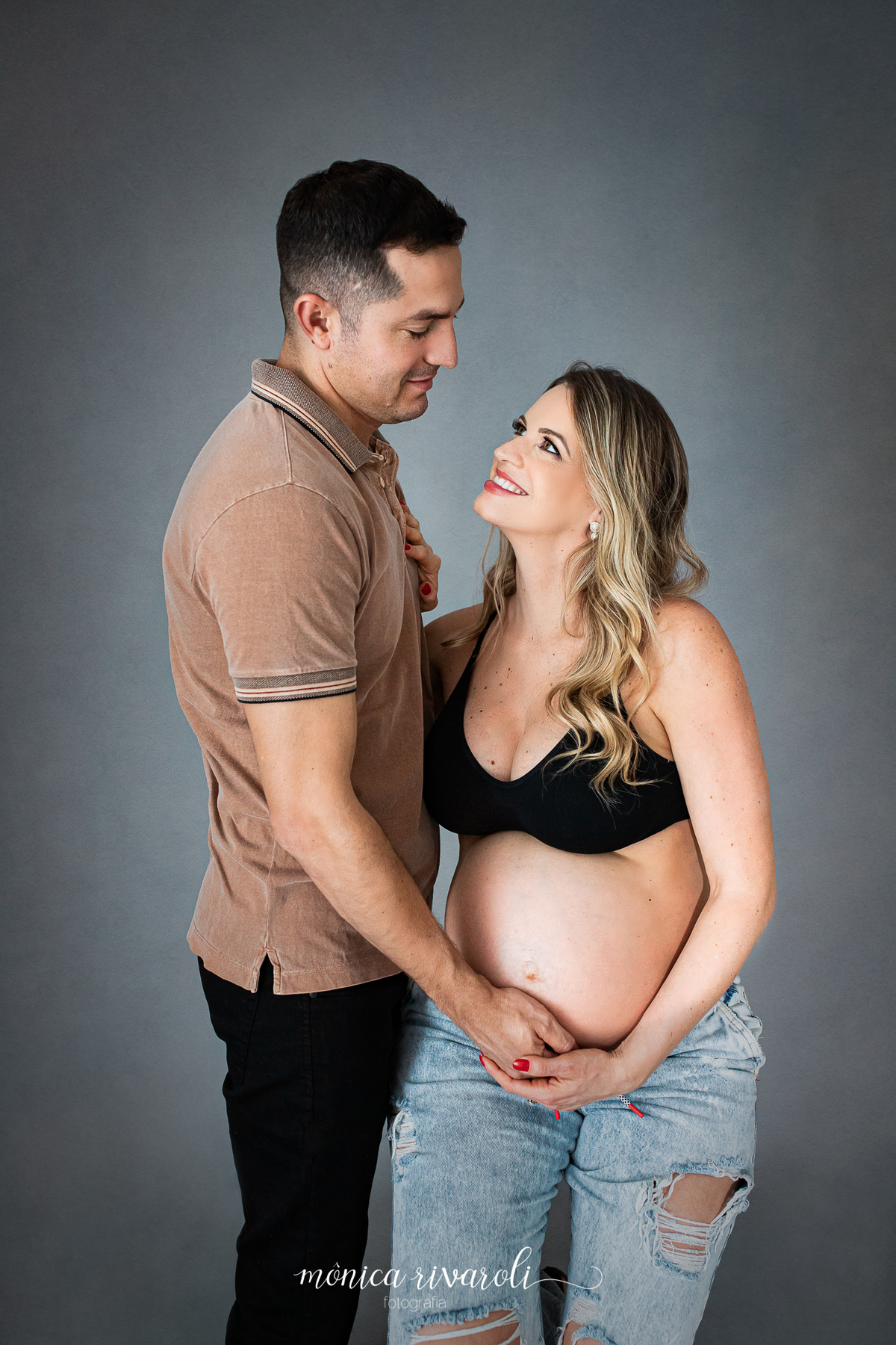 Ainda sentada no banquinho, agora o papai está ao seu lado, com a mão na barriga da mamãe. Eles se olham e a mamãe sorri. 