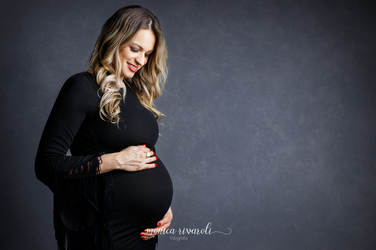 Ainda no mesmo cenário, agora a gestante tem as duas mãos na barriga, uma sobre e outra embaixo. Ela olha para o bebê e sorri. 