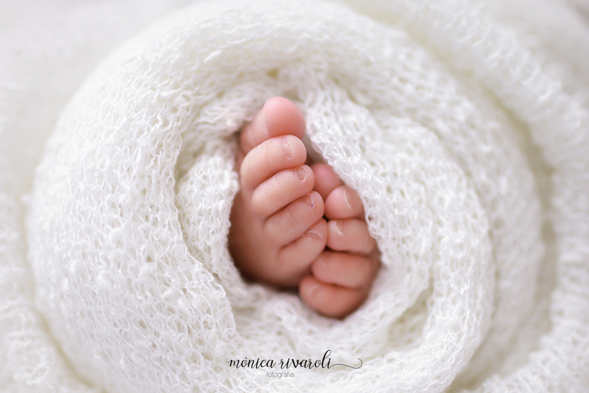 Nesta foto, os pezinhos da neném estão enroladinhos em um prop branco.  