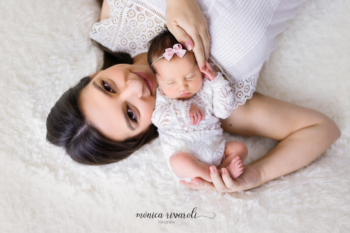 Ainda na manta de pelinhos, agora só a mamãe com a neném, ela esta deitada de ponta cabeça, enquanto a bebê dorme no seu ombro. Uma das suas mãos está na cabecinha da bebê e a outra segura os pezinhos cruzados dela. 