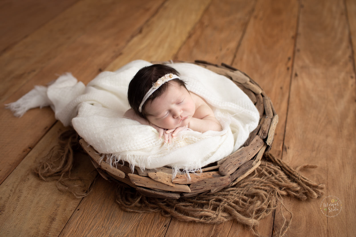 Foto feita para ensaio newborn em studio localizado no Bela Vista  - São Paulo, SP. Na foto a bebê está dentro de uma tronquinho de madeira, com as mãos embaixo do queixo e uma tiara