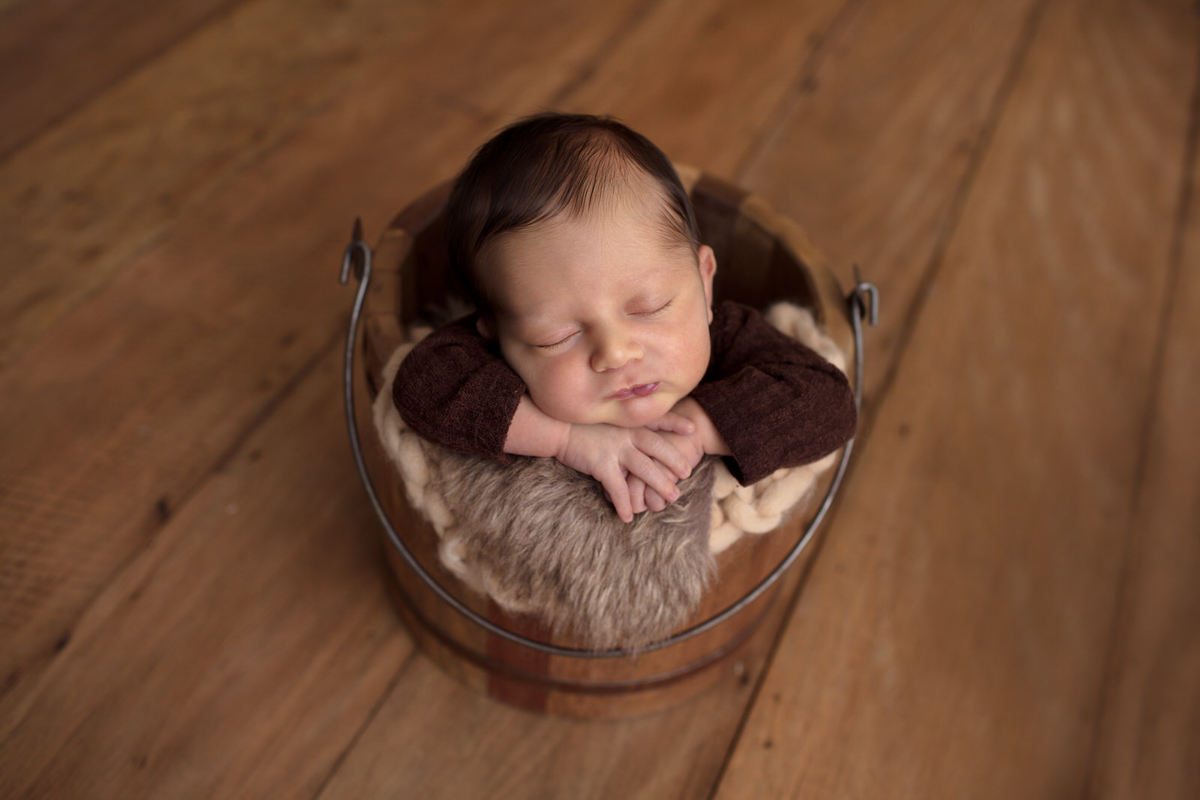 Fotos feitas em studio localizado na Vila Madalena - São Paulo, SP. Na foto o bebê está dentro de um balde de madeira com os bracinhos embaixo do queixo