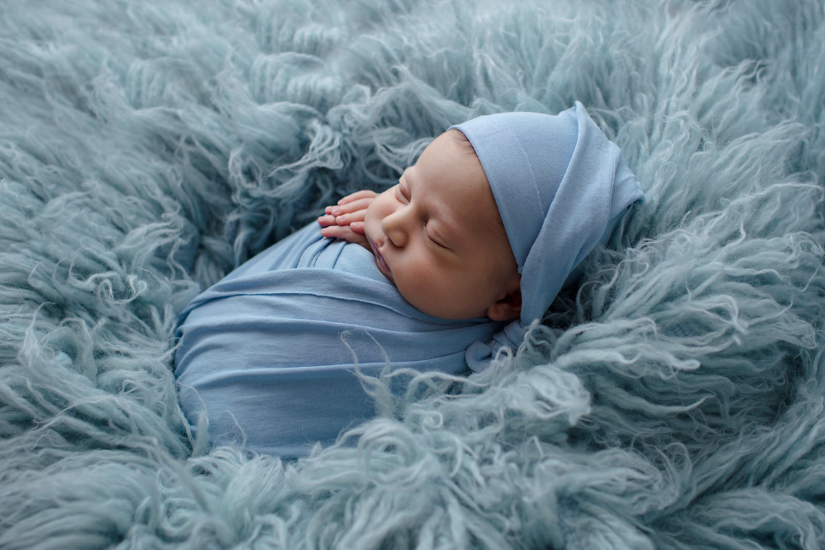 Foto feita para ensaio newborn do Arthur de 11 dias, em studio localizado em Perdizes - São Paulo, SP. Na foto o bebê está deitado em um tapete azul claro enrolado em um wrep azul como um saquinho de batatas. 