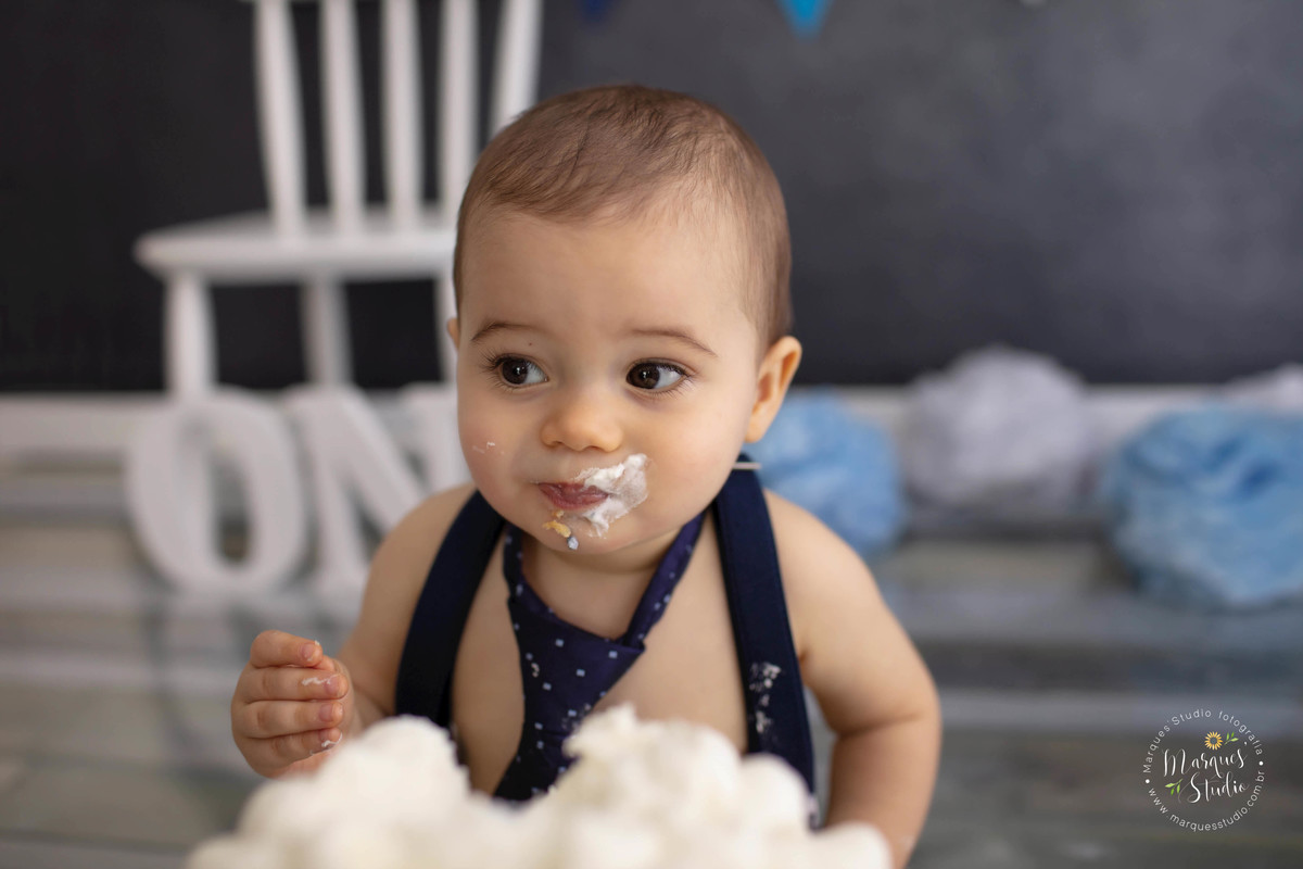 Fotografia de bebê de 1 ano comendo um delicioso bolo no ensaio Smash The Cake no studio na Vila Madalena São Paulo SP com bolo em sua mão e em sua boca