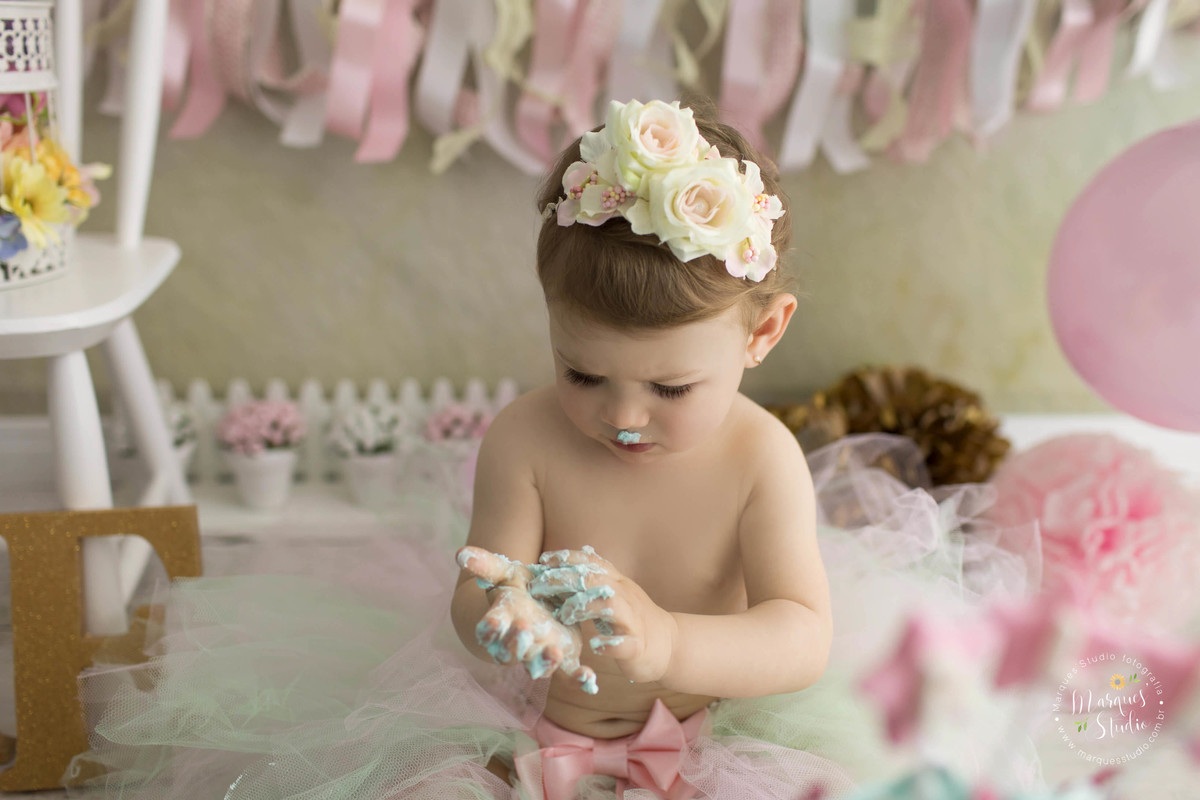 Foto feita para o smash the cake de menina, em studio fotográfico na Vila Leopoldina São Paulo SP com o tema jardim na cor Tiffany com bolo personalizado a bebê esta usando uma coroa com flores na cabeça ela está experimentando o delicioso bolo