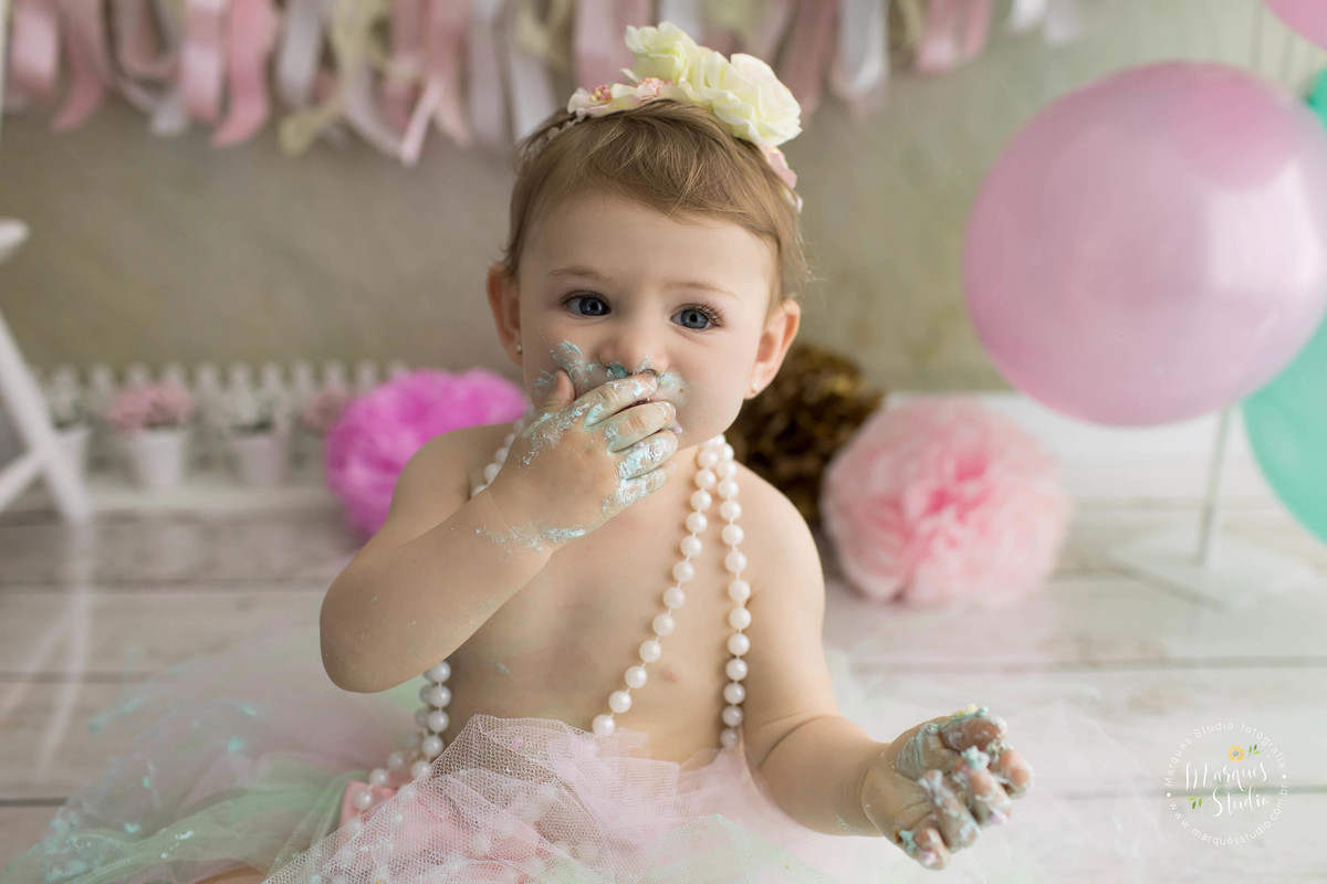 Esse lindo ensaio foi realizado no estado de São Paulo SP onde as fotos foram feitas em studio fotográfico na Vila Madalena SP a bebê menina está com uma linda coroa de flores na cabeça e com um lindo colar de pérolas e está comendo bolo do smash the cake