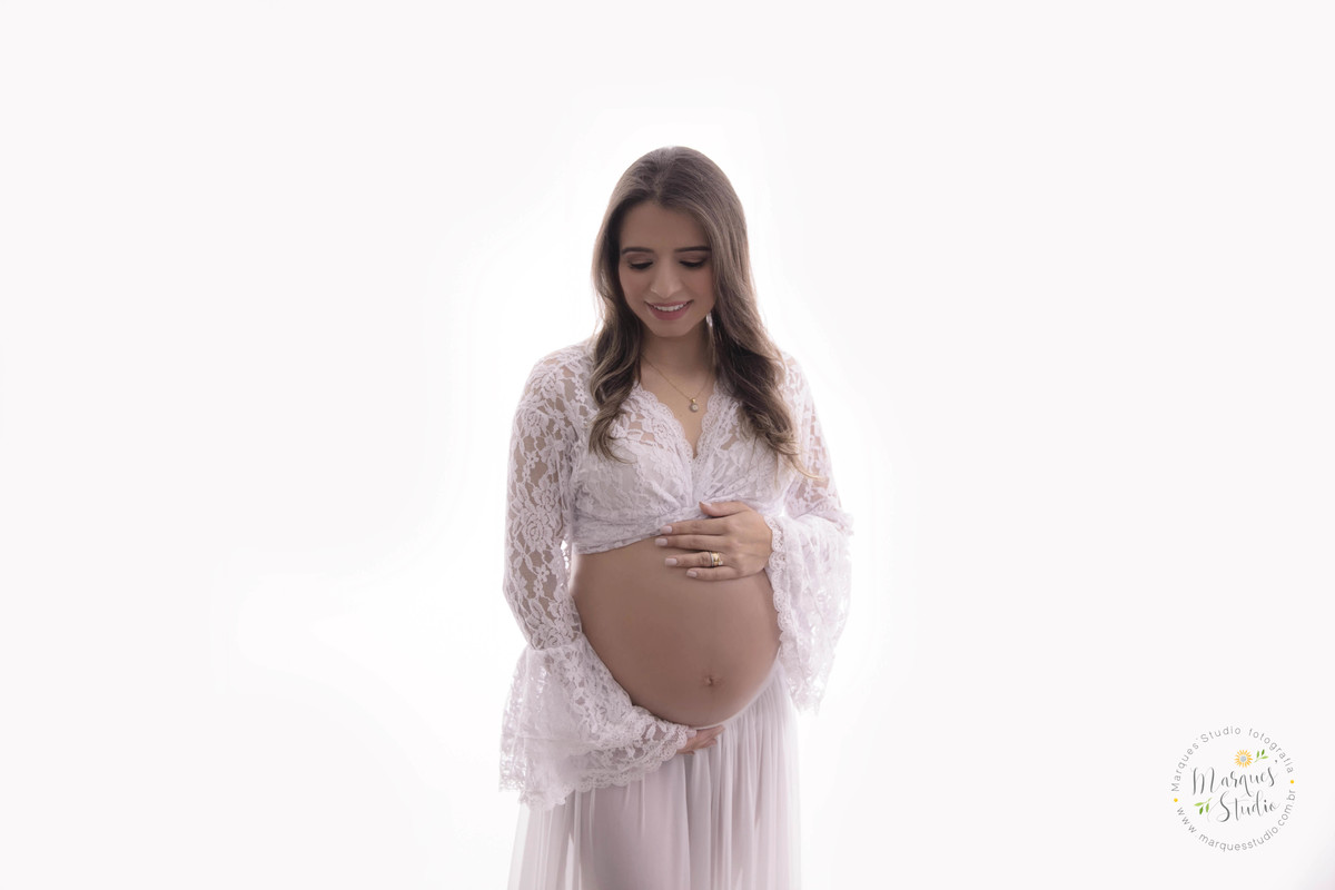 Gestante linda em seu ensaio fotográfico no studio localizado em Osasco São Paulo SP com o olhar para o seu bebê sorrindo com as duas mãos sobre sua barriga em um lindo fundo fotográfico infinito branco