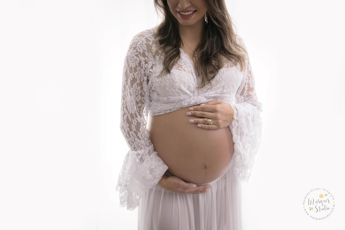 Foto feita para o ensaio fotográfico da gestante Priscilla no studio de fotografia na Vila Madalena São Paulo SP a gestante está sorrindo com as mãos sobre a barriga com muita ternura e carinho olhando para os seus Bebês