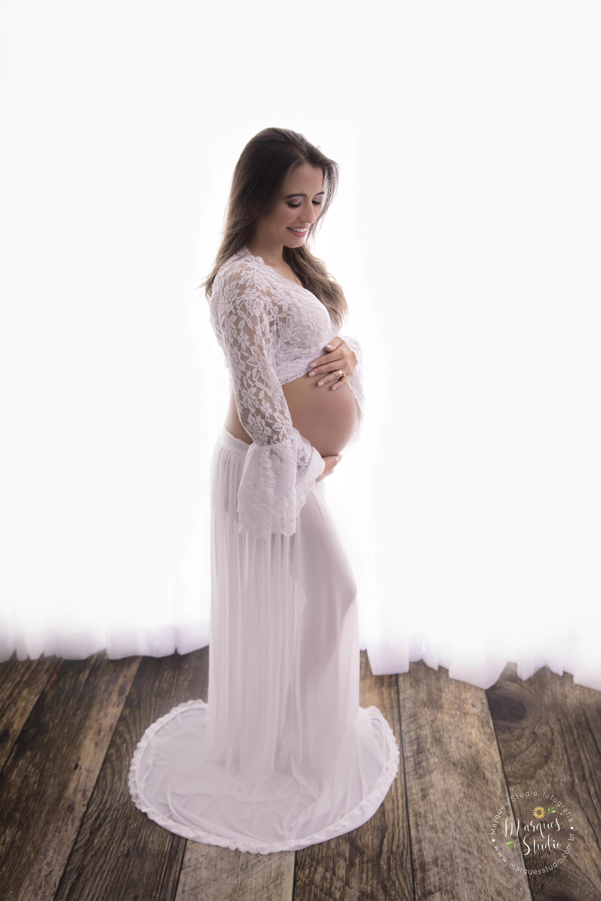 Fotografia feita no studio fotográfico localizado na Vila Leopoldina São Paulo SP nesta foto a gestante está de perfil com as mãos sobre a barriga com um lindo conjunto de saia e top branco com detalhe podemos ver sua barriga de perfil