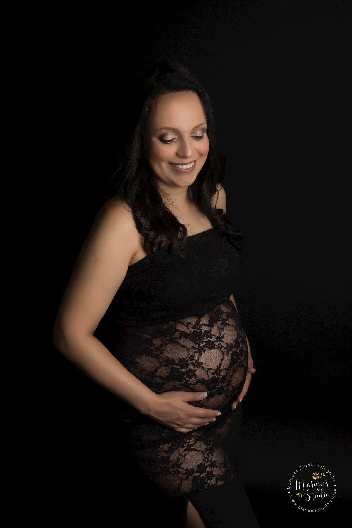 Foto feita para o ensaio da gestante Eliane no studio de fotografia em Osasco São Paulo SP Ela está usando um lindo vestido preto com detalhes em renda, ela está com as mãos sobre a sua barriga de gestante, com um lindo sorriso em seu rosto