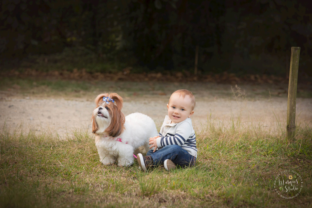 Foto Feita para a sessão Smash The Cake em studio na zona Oeste, Osasco, SP de criança de 1 ano sorrindo sentada na linda grama verde, com sua bela cachorrinha, ao fundo uma maravilhosa paisagem verde.