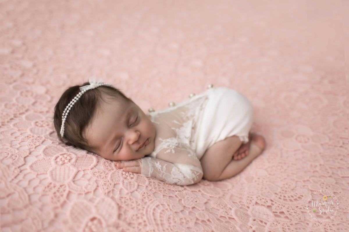 Fotografia de bebê recém-nascido menina, deitada no puff com as mãozinhas no rosto, foto feita em studio fotográfico na Vila Perdizes, São Paulo, SP, ela está dormindo e usando uma linda roupinha branca com renda.