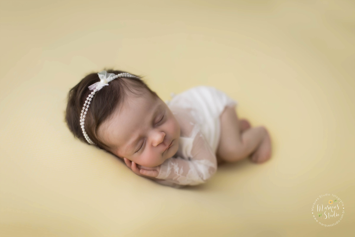 foto de recém-nascido usando roupinha branca com detalhes em renda no puff, feita em estúdio fotográfico na Vila Leopoldina, São Paulo, SP, ela está dormindo com as mãozinhas no rosto.