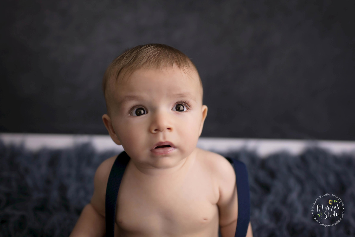 Foto Feita para a sessão de acompanhamento infantil em studio na zona Oeste, Sumaré, São Paulo, SP, de uma criança de 6 meses sorrindo, ele está sentado em um lindo tapete azul marinho, e o fundo fotográfico também é na cor azul marinho.