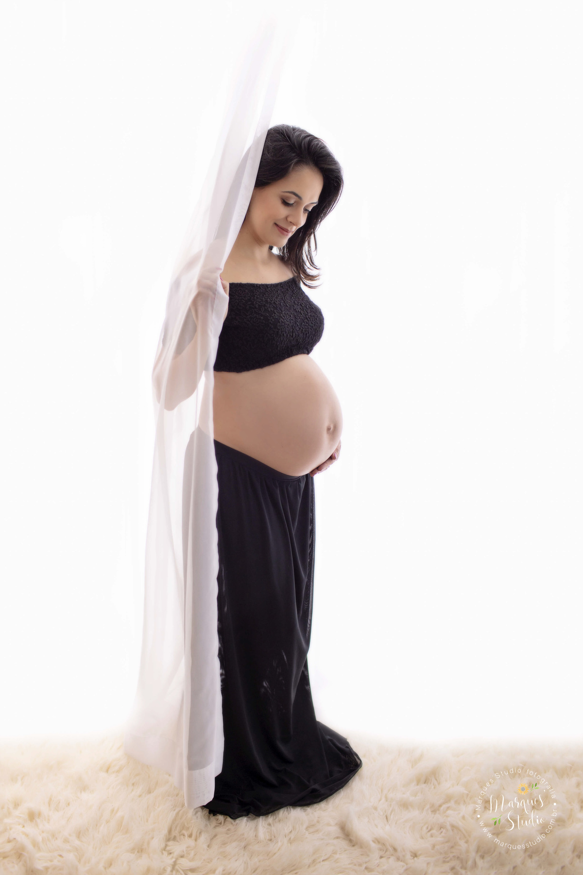 Foto feita em studio fotográfico localizado na Vila Leopoldina São Paulo SP para o ensaio gestante da Renata Secco, ela está usando um lindo conjunto de top e saia preto ela está posicionada de perfil e sua mão esquerda está sobre sua barriga de gestante.