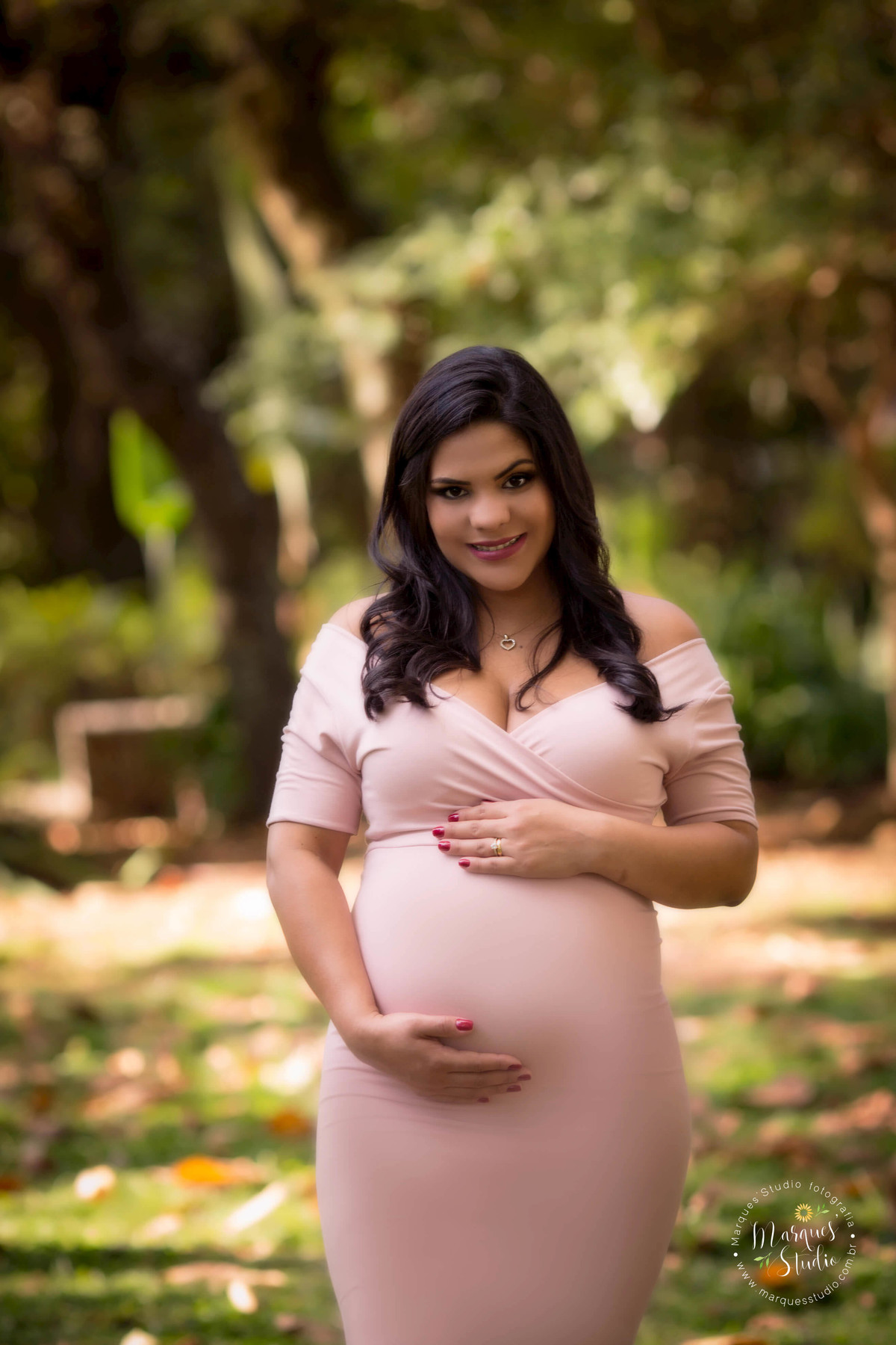 Foto feita na região Oeste de São Paulo SP Vila Madalena para ensaio gestante da Thamyres, ela está usando um belo vestido rosa com as mãos sobre a barriga dando um lindo sorriso suas unhas estão pintadas na cor vermelha, ao fundo tem uma linda arvore.