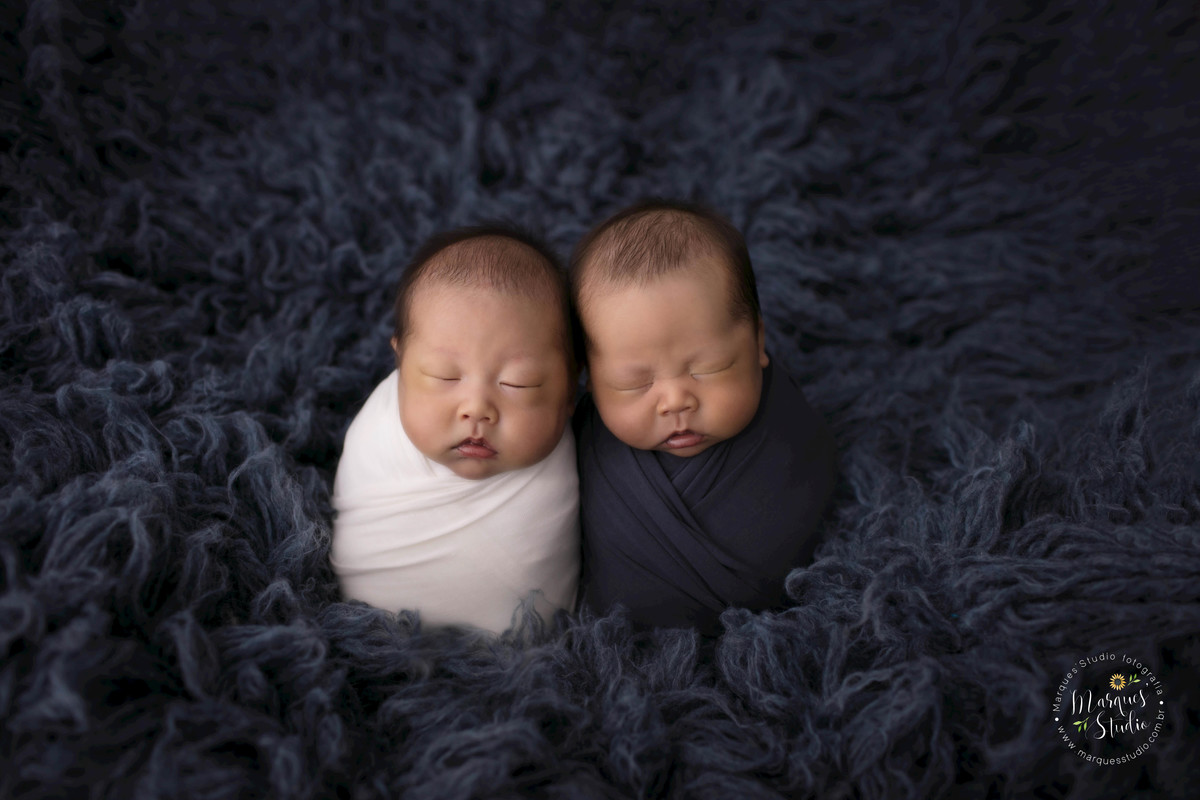Fotografia dos bebês recém-nascidos Pedro e Davi no wrap azul marinho e bege. Foto feita em Estúdio no Morumbi, São Paulo, SP, eles estão dormindo um do lado do outro, fotos de gêmeos, gêmeos recém-nascidos, fotografia de gêmeos em São Paulo, SP.