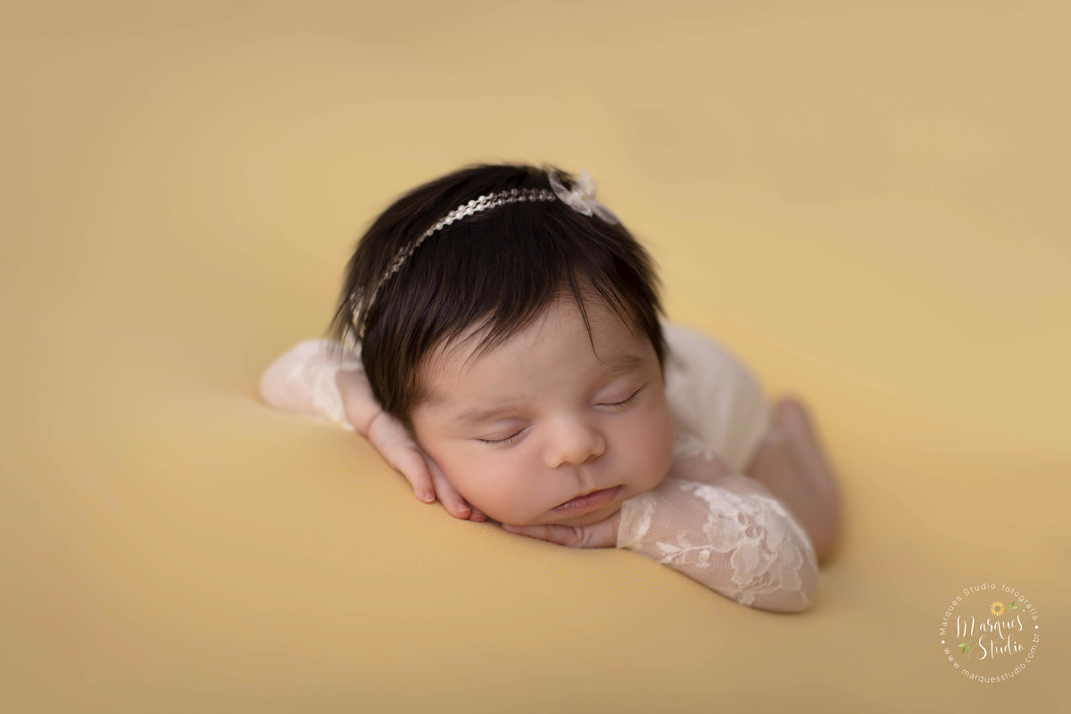 Fotografia de bebê menina, deitada no puff com as mãos no rosto, foto feita em studio fotográfico na Avenida Paulista, São Paulo, SP, ela está dormindo e usando um lindo macacão na cor branca com renda, e no cabelo uma linda headband de lacinho branco.