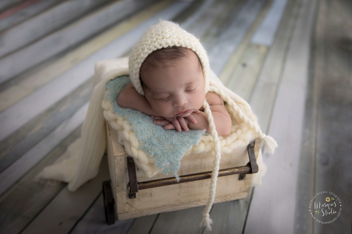 fotografia de bebê em vagãozinho, com roupa e touca na cor bege, em um fundo de madeira. Foto feita em Estúdio na zona sul São Paulo - SP, para o ensaio Newborn do Davi de 15 dias.