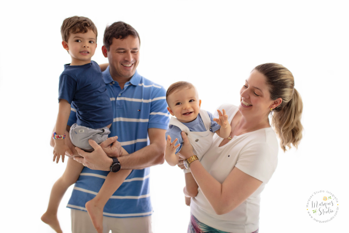 Fotografia da sessão de acompanhamento do bebê Leo com a mamãe o papai e o irmãozinho em um fundo fotográfico branco, a família está sorrindo no studio localizado na Vila Leopoldina, São Paulo, SP.