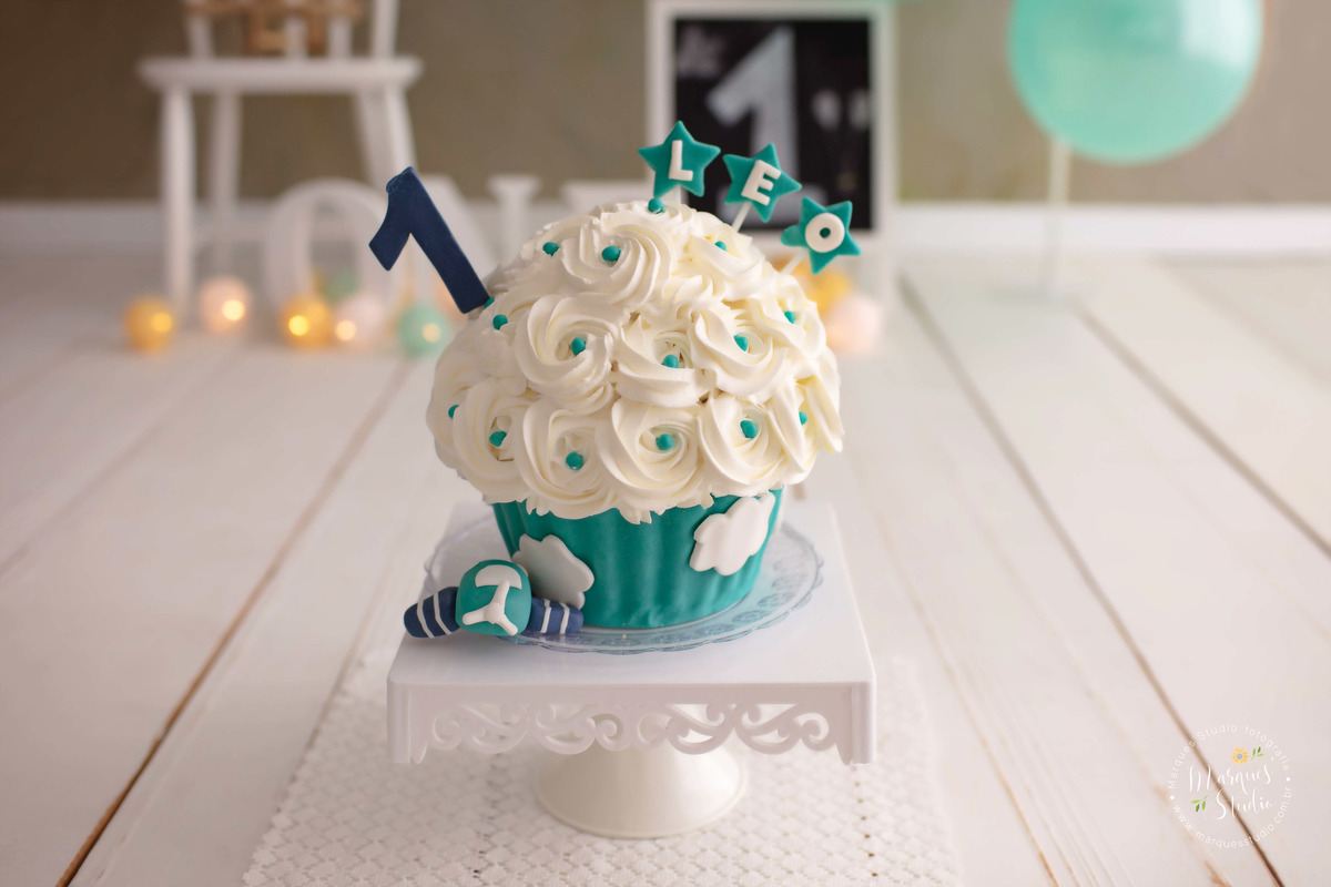 Fotografia feita para a sessão smash the cake do Leo, com uma linda decoração nas cores verde claro e branco, na frente temos um lindo bolo decorado com nuvens e um aviãozinho, ao fundo bandeirinhas e balões na cores branco e verde, na Vila Madalena, SP. 