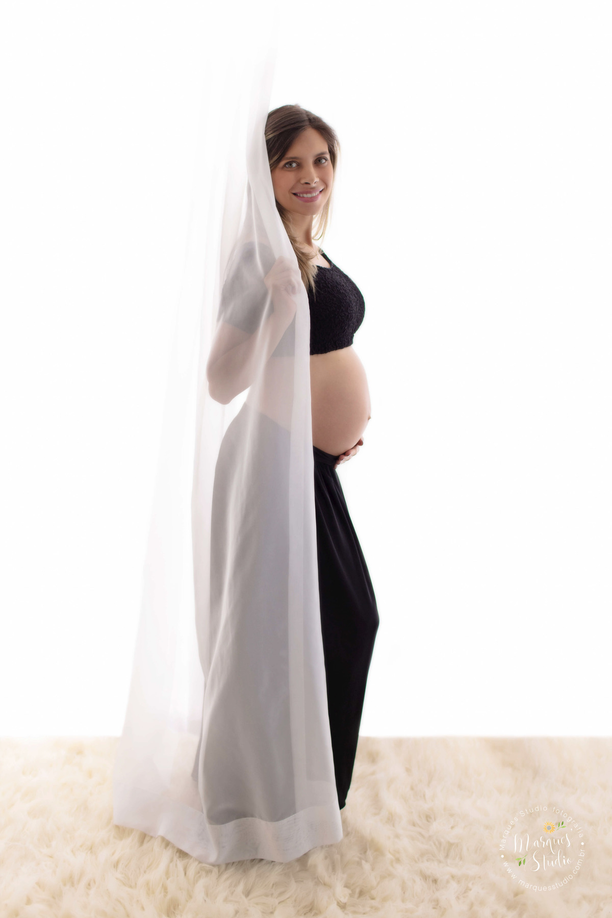 Foto feita em studio fotográfico localizado na Vila Leopoldina São Paulo SP para o ensaio gestante da Camila, ela está usando um lindo conjunto de top e saia preto, ela está posicionada de perfil e sua mão esquerda está sobre sua barriga de gestante.