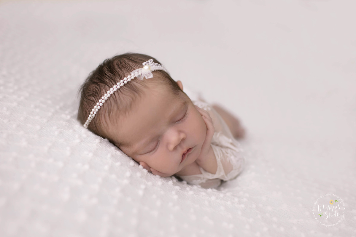 Foto de bebê menina, deitada no puff com uma manta branca de bolinhas, com as mãos no rosto, foto feita em studio fotográfico localizado na Vila Leopoldina, São Paulo, SP, ela está dormindo e usando um lindo macacão na cor branca com renda.