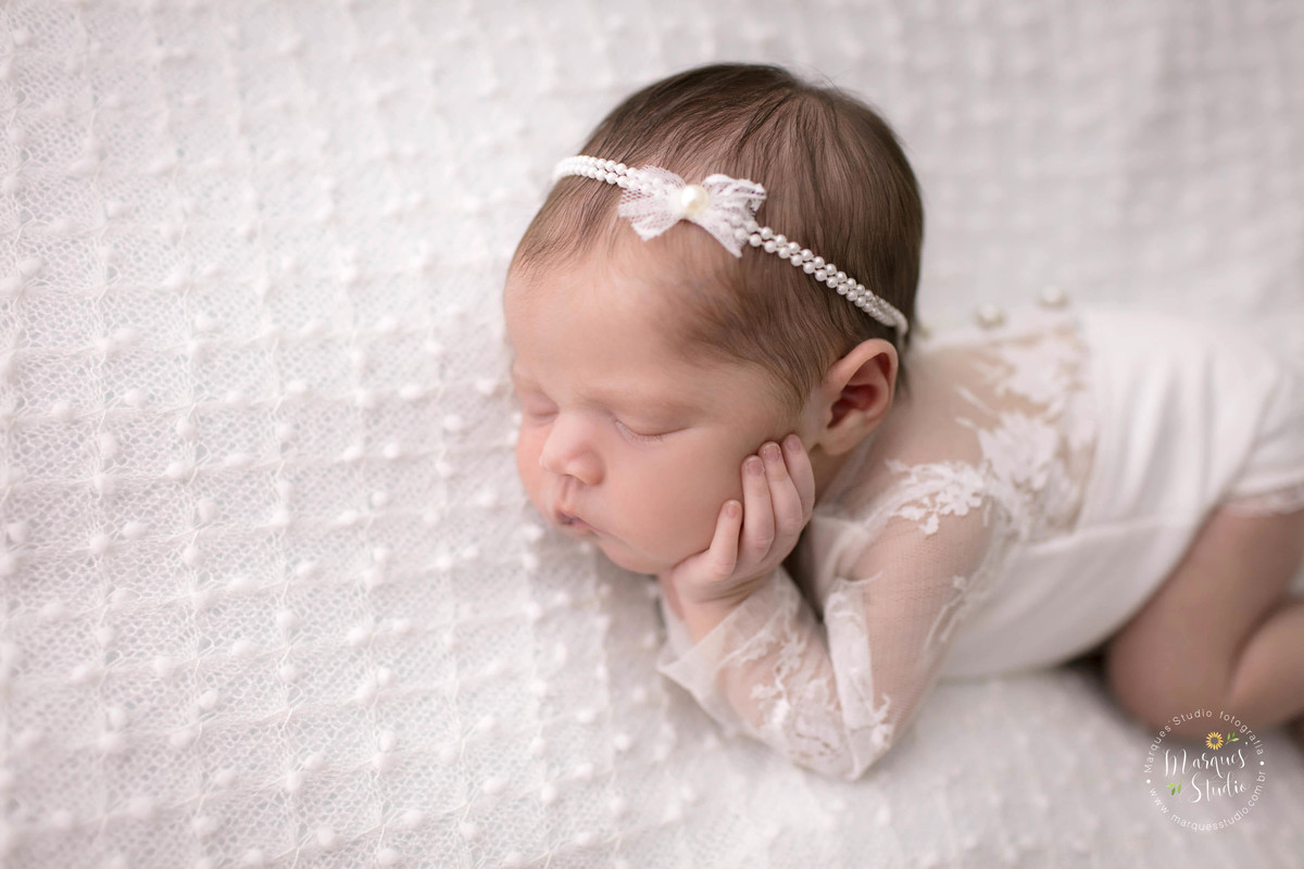 Foto de bebê menina, deitada no puff com uma manta branca de bolinhas, com as mãos no rosto, foto feita em studio fotográfico localizado na Vila Madalena, São Paulo, SP, ela está dormindo e usando um lindo macacão na cor branca com renda.