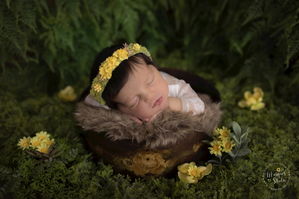foto de bebê recém-nascida  no jardim, realizado no nosso studio fotográfico em São Paulo SP Vila Madalena, a bebê está dormindo com as mãozinhas no rosto, em sua cabeça ela usa uma linda headband de florzinhas amarelas, e um lindo macacão branco de renda