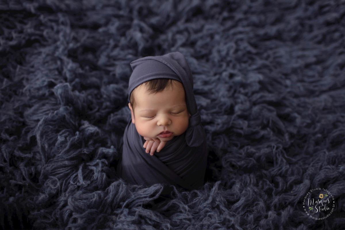 Fotografia de bebê recém-nascido no wrap de cor azul marinho. Foto feita em Estúdio na zona sul São Paulo - SP, do ensaio Newborn do Thomas, ele está dormindo em um flokat azul marinho, com as mãozinhas no rosto.