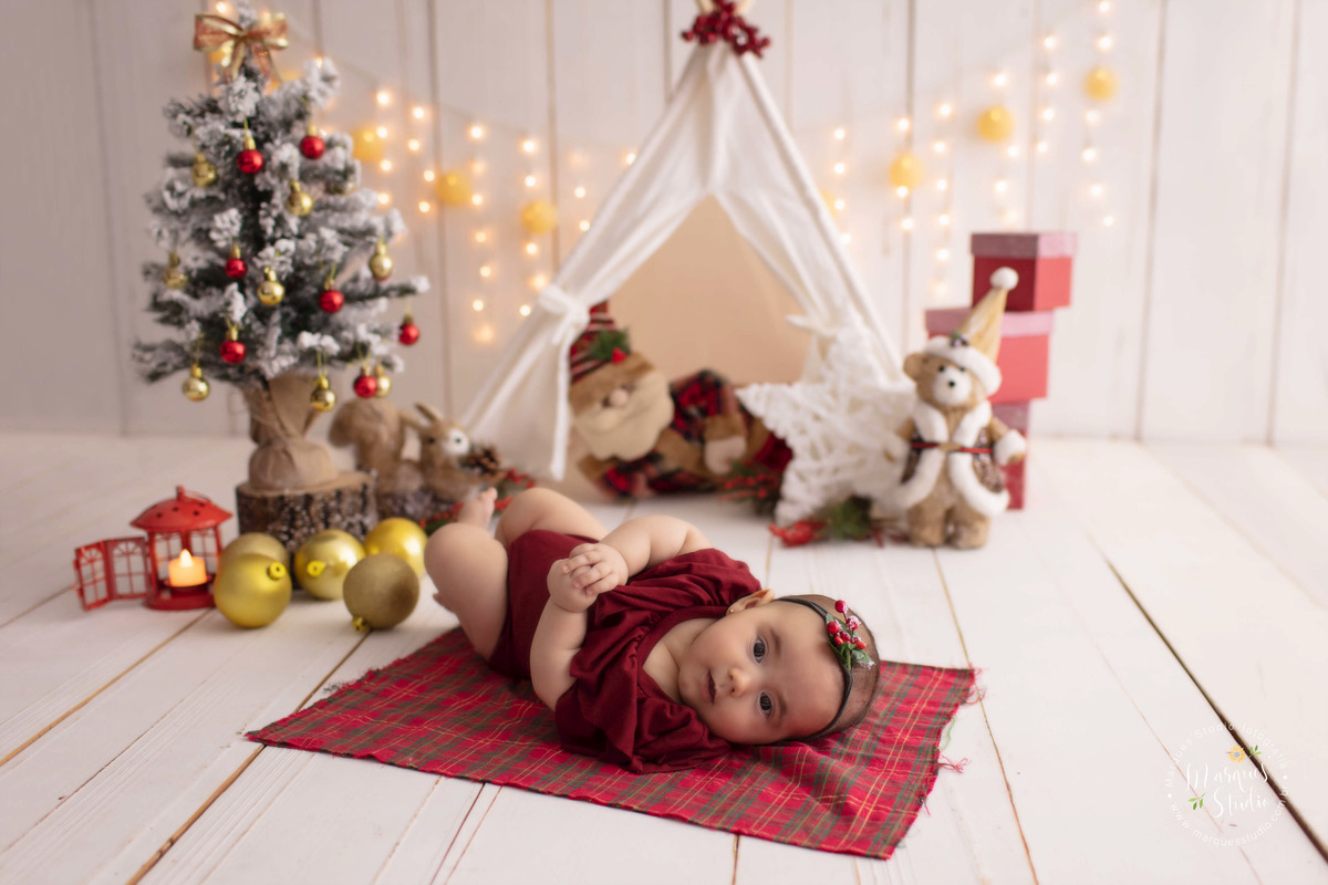 Foto feita no studio fotográfico localizado na Avenida Paulista, São Paulo, SP, para o ensaio de natal da Bia, na foto ela está em um belo cenário com papai Noel, arvore e luzinhas de natal, com caixinhas de presentes, ela está usando um macacão vermelho.