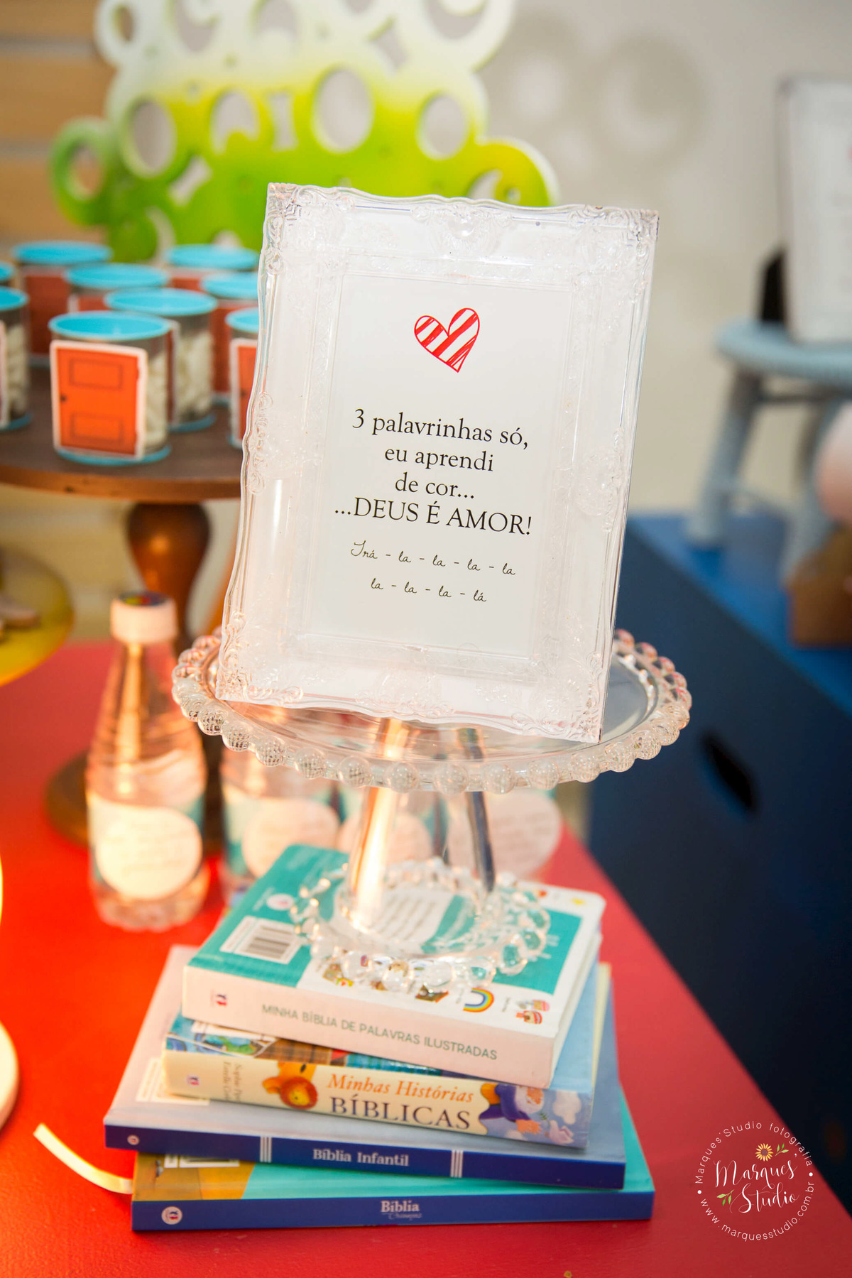 Fotografia tirada no aniversário de 1 ano do Benjamin, na foto temos alguns livros sobre Jesus e um quadro com a letra da música das três palavrinhas. Buffet está localizado na Av. Paulista em São Paulo, SP