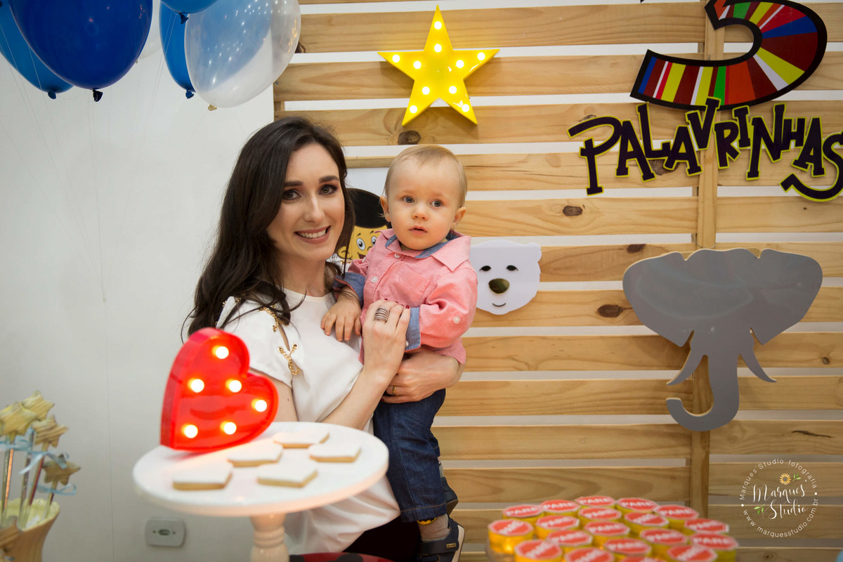 Fotografia tirada no aniversário do Benjamin de 1 ano, na foto temos o aniversariante no colo da sua mamãe. Eles estão atrás da mesa do bolo. O buffet está localizado na Zona Sul de São Paulo - SP
