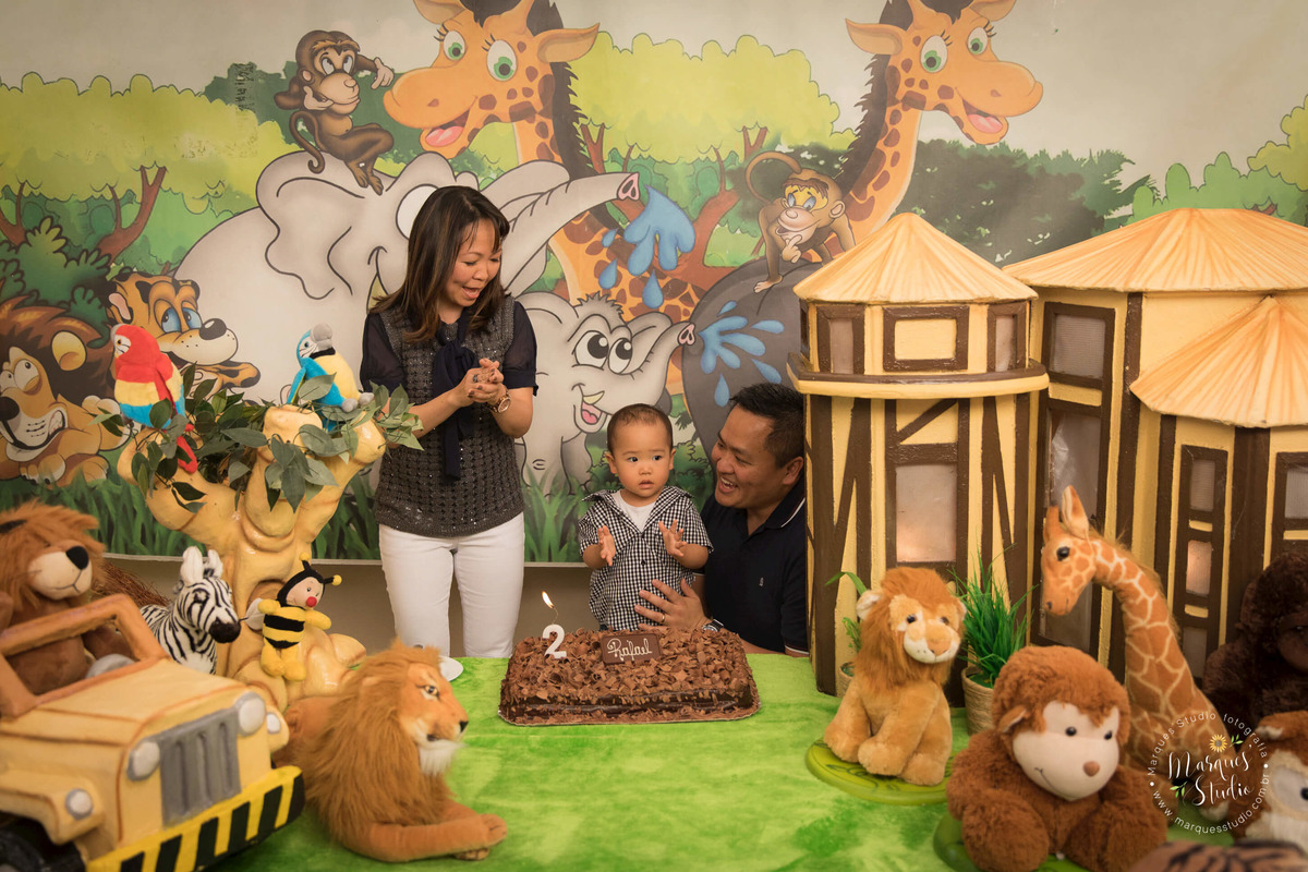 Foto registrada no aniversário de 2 anos do Rafael, em um buffet localizado na Consolação - São Paulo, SP. Na foto temos a família com o aniversariante atrás da mesa do bolo cantando parabéns. O tema da festa foi safari.