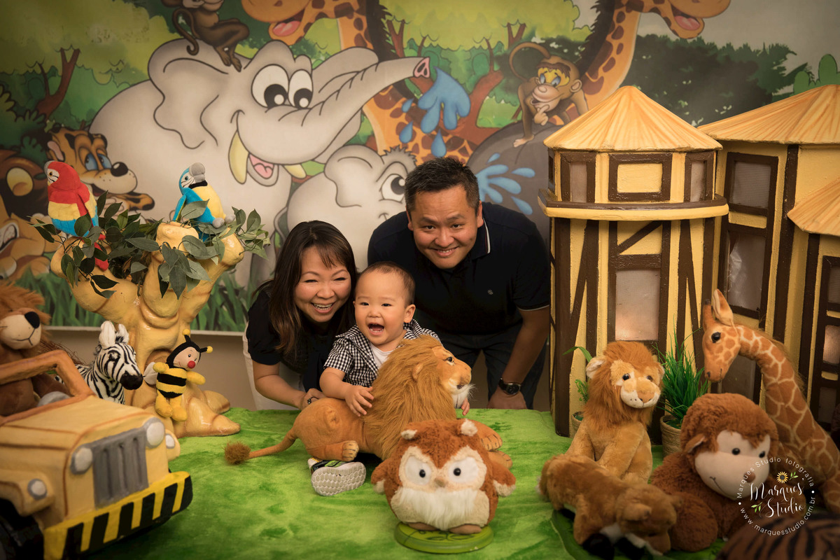 Foto registrada no aniversário de 2 anos do Rafael, em um buffet localizado em Osasco - São Paulo, SP. Na foto temos a família com o aniversariante atrás da mesa do bolo sorrindo. O tema da festa foi safari.