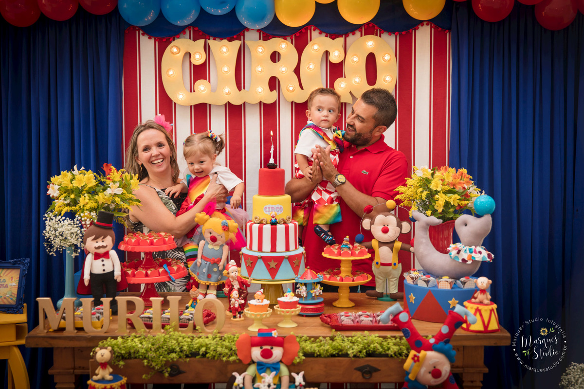 Foto registrada no aniversário de um aninho dos gêmeos Murilo e Giovanna. Na foto temos os aniversariantes no colo da mamãe e do papai, eles estão atrás da mesa do bolo cantando os parabéns. Buffet localizado na Consolação - São Paulo, SP
