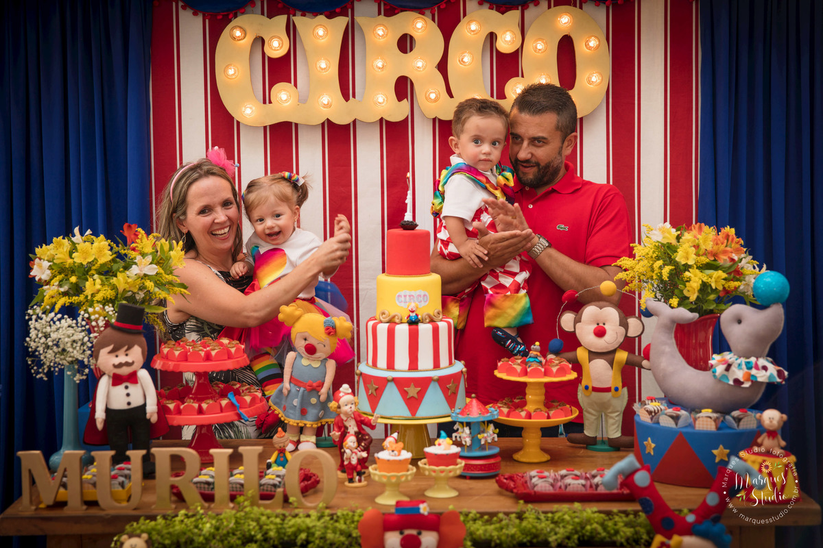 Foto registrada no aniversário de um aninho dos gêmeos Murilo e Giovanna. Na foto temos os aniversariantes no colo da mamãe e do papai, eles estão atrás da mesa do bolo cantando os parabéns. Buffet localizado na Vila Madalena - São Paulo, SP