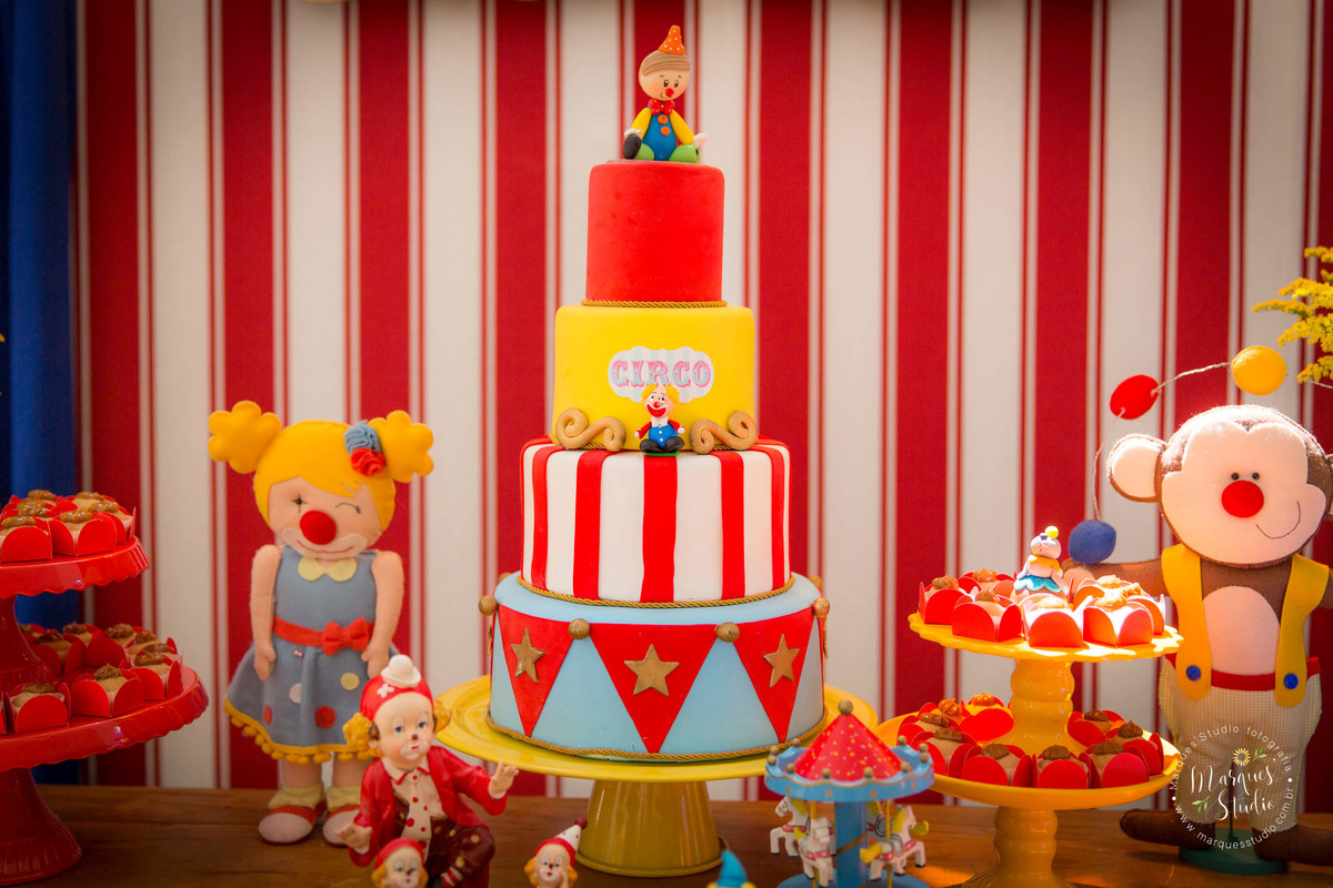 Fotografia tirada no aniversário dos gêmeos Murilo e Giovanna em Pinheiros - São Paulo, SP. Na foto temos a mesa do bolo decorada com o tema circo, com animais de pelúcia, muitos docinhos e um lindo bolo.