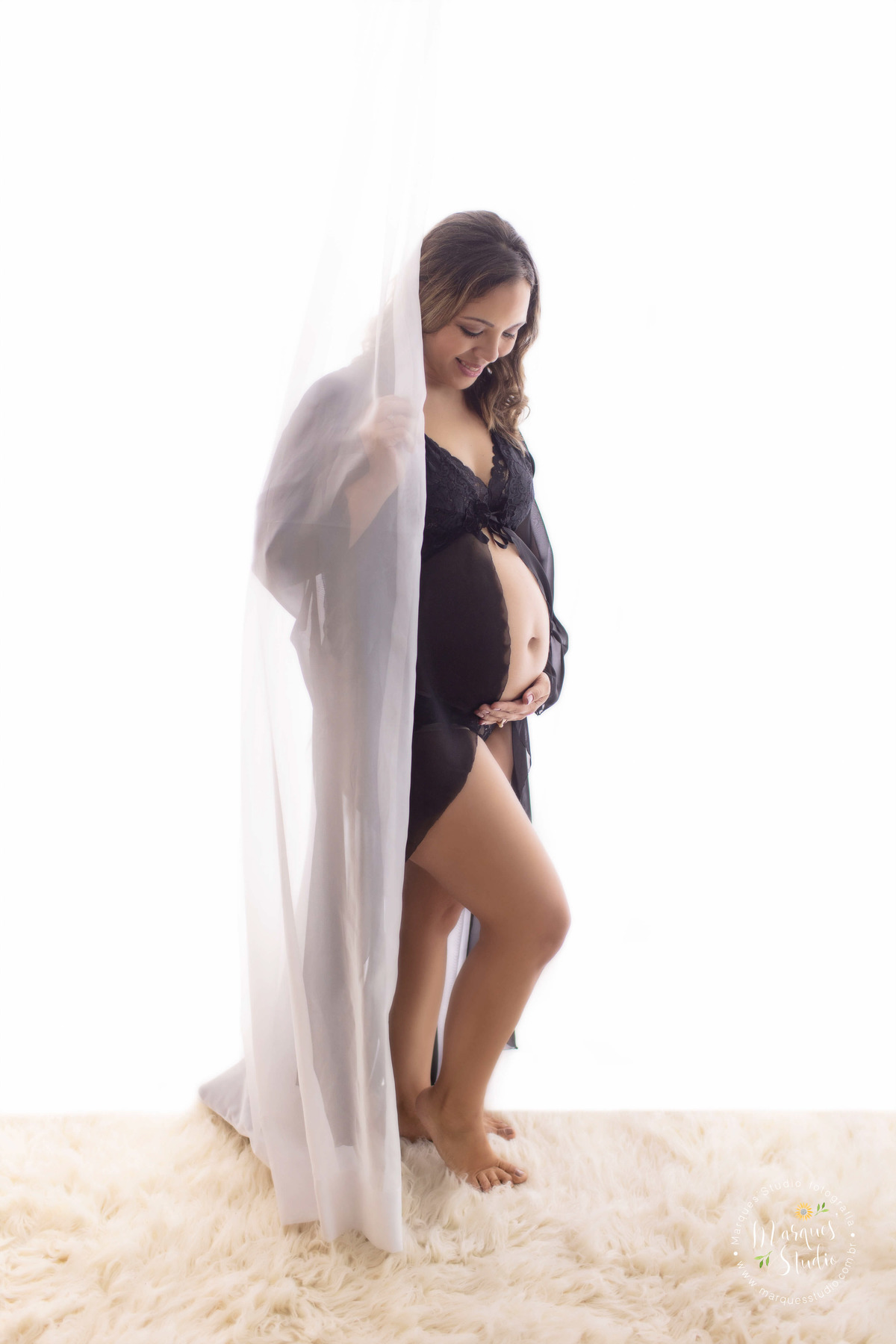 Foto feita para o book gestante da Erika. Ela está usando uma linda camisola preta, com a mão na barriga e atrás de uma cortina branca . O studio está localizado em Sumaré - São Paulo, SP.