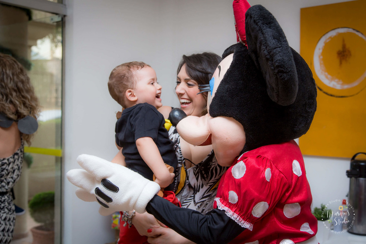 Foto registrada na festinha de dois anos do Guilherme. Na foto temos a  mamãe carregando o Gui no colo enquanto um animador vestido de Minie fala com ele. O Guilherme está muito feliz e animado. O buffet se encontra em Perdizes - São Paulo, SP.